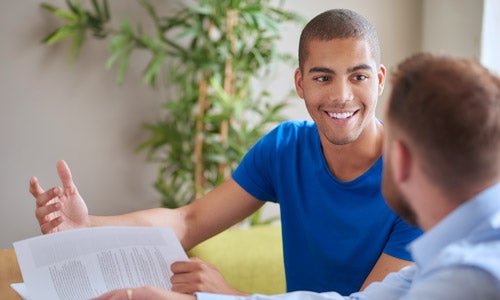A young male student smiles while reviewing financial aid documents with an advisor.